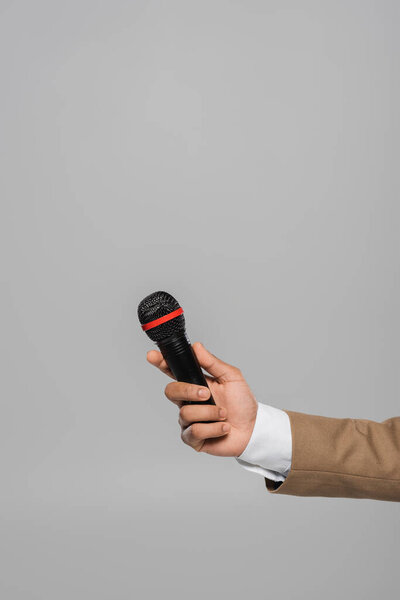 Cropped view of young event host in blue jacket and white shirt holding wireless microphone while standing isolated on grey with copy space 