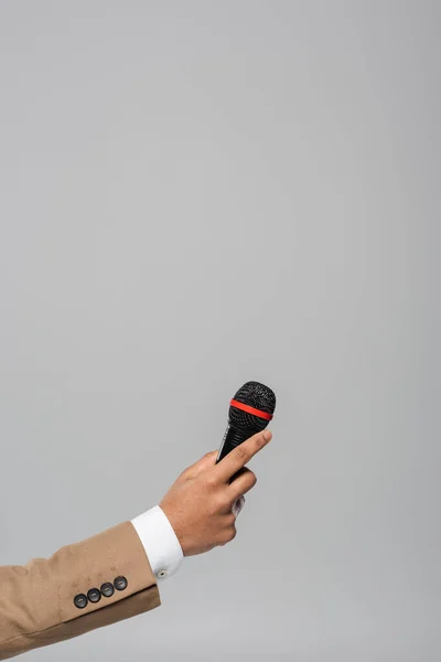 Cropped view of hand of event host in brown jacket holding wireless microphone during performance isolated on grey with copy space