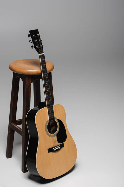 Acoustic guitar standing near brown wooden chair on grey background with copy space 