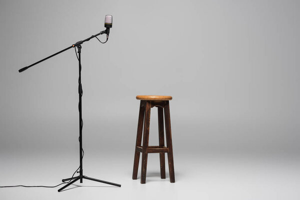 Brown wooden chair standing near microphone with wire on stand on grey background with copy space, high stool in studio 