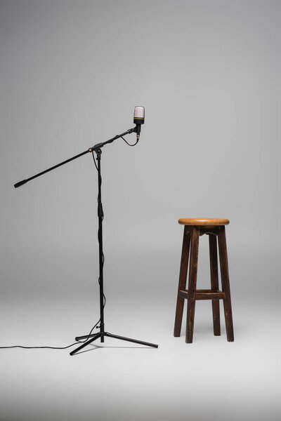 Brown wooden chair standing near black microphone on metal stand on grey background with copy space, high stool in studio 