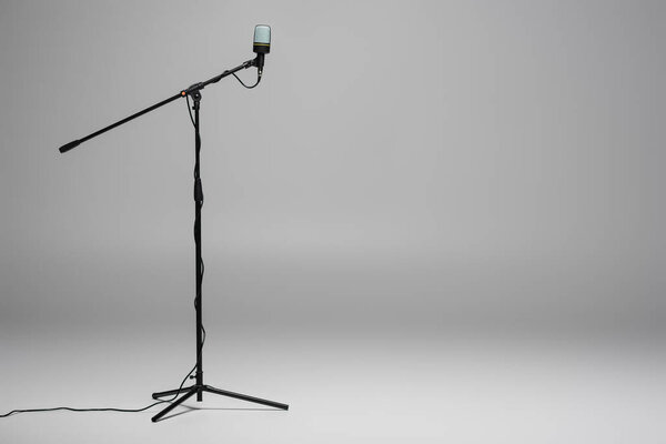 Black microphone with wire on metal stand on grey background with copy space 
