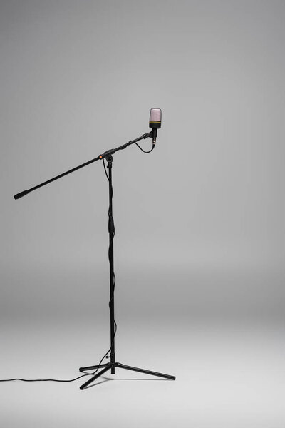 Black microphone with wire on stand on grey background with copy space, studio shot 