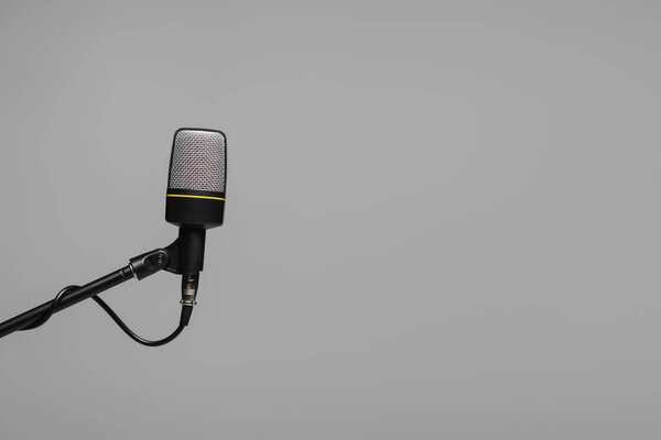 Microphone with wire on black metal stand isolated on grey with copy space, studio photo 