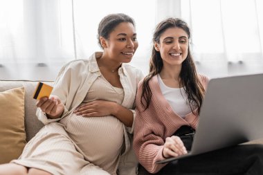 Mutlu lezbiyen partnerle online alışveriş yaparken elinde kredi kartı tutan hamile bir kadın. 