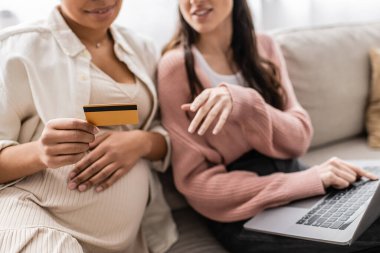 Lezbiyen partnerle online alışveriş yaparken elinde kredi kartı tutan hamile kadının kısmi görüntüsü 