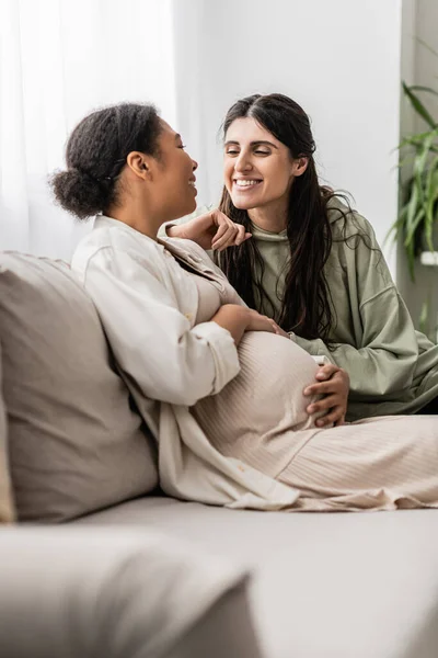 Feliz Lesbiana Mujer Abrazando Embarazada Multirracial Esposa Mientras Sentado Sofá — Foto de Stock