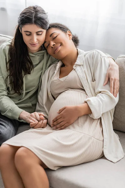 Feliz Lesbiana Mujer Abrazando Embarazada Multirracial Esposa Mientras Sentado Sofá — Foto de Stock
