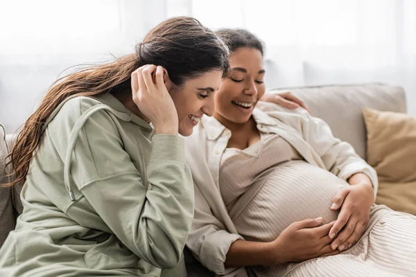 Feliz Lesbiana Sonriendo Mientras Abrazando Embarazada Multirracial Esposa Mientras Sentado — Foto de Stock