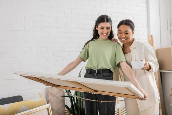 Cheerful Interracial Lgbt Couple Looking Painting While Standing New House — Stock Photo, Image