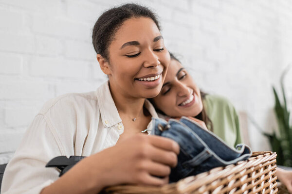 веселая лесбиянка, облокотившаяся на плечо улыбающейся многорасовой подружки, складывающей одежду 