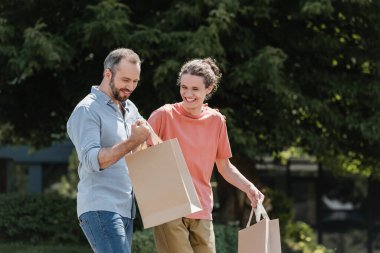 cheerful father and son walking with shopping bags outdoors  clipart