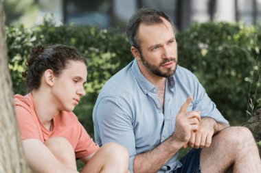 Sakallı baba, genç oğlunun yanına oturmuş yeşil parkta konuşuyor. 