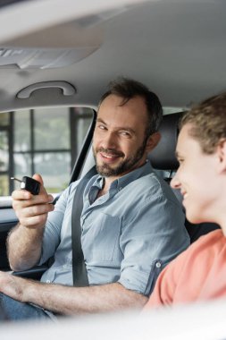 Neşeli ve sakallı bir adam modern otomobilde oğlunun yanında araba anahtarı tutuyor. 