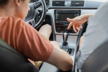 father pointing at changing gear handle while teaching son how to drive car  clipart