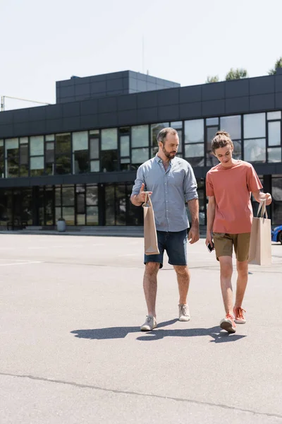 Bärtiger Vater Und Teenager Sohn Laufen Mit Einkaufstüten Aus Einkaufszentrum — Stockfoto