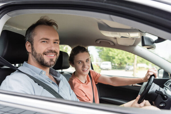 happy father and teenage son looking at camera while sitting together in car 