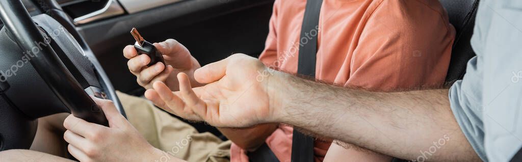 Cropped view of father giving car key to teenage son sitting next to steering wheel, banner