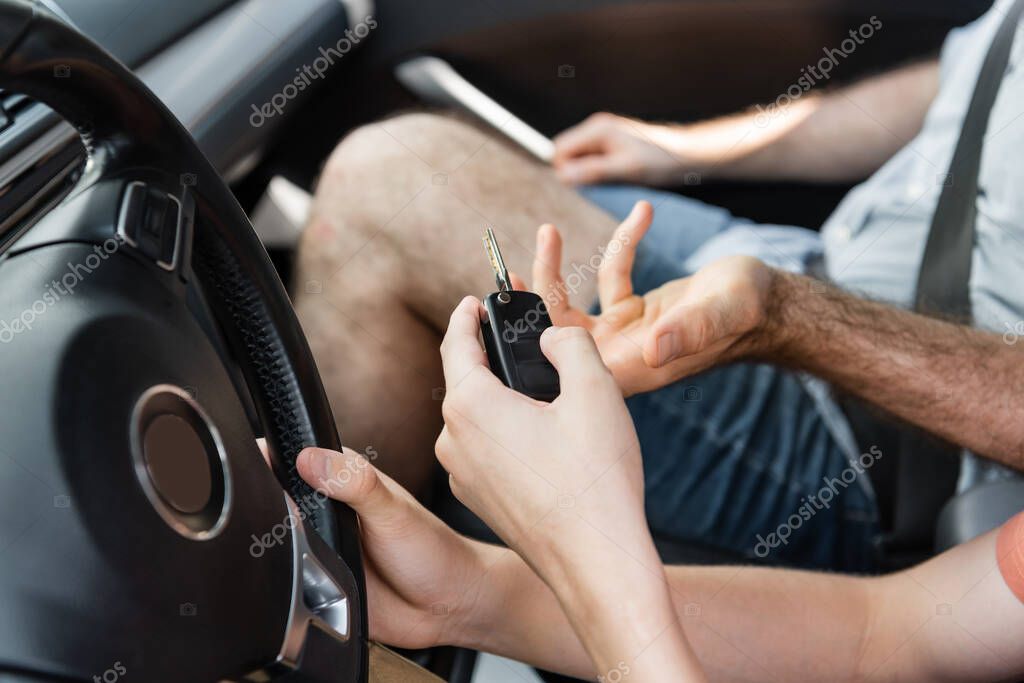 Cropped view of teenage boy holding car key next to father in automobile