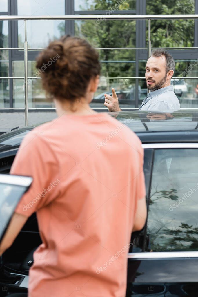 Bearded father pointing at teenage son while standing together near modern car