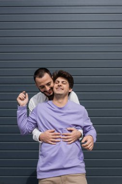 Neşeli ve sakallı homoseksüel bir adam. Parmaklıklı esmer partnere sarılıyor. Gülüyor. 
