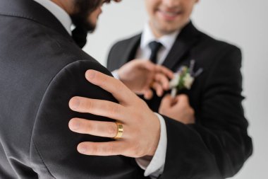 Bulanık görüşlü, altın yüzüklü, klasik takım elbiseli, gri renkte izole edilmiş düğün kutlaması sırasında eşinin omzuna dokunan eşcinsel bir adam.  