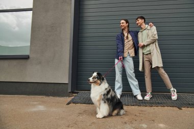 At kuyruklu neşeli eşcinsel adam, elinde Avustralya çoban köpeği tasması ve gülen erkek arkadaşına sarılırken sokakta garaj kapısının yanında yan yana dikiliyordu.