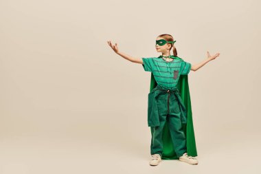 Yeşil pelerinli, maskeli, süper kahraman kostümlü güçlü bir kız uzanmış elleriyle ayakta duruyor ve gri arka planda Uluslararası Çocuk Günü 'nü kutluyor. 