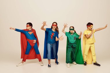 Renkli süper kahraman kostümlü çok kültürlü çocuklar. Gri arka planda, stüdyoda, Uluslararası Çocuk Günü konseptinde birlikte hareket ediyorlar.