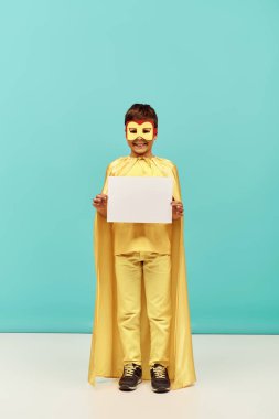 Sarı süper kahraman kostümlü, maskeli, mavi arka planda boş kağıtları olan, Uluslararası Çocuk Koruma Günü konsepti olan çok kültürlü, pozitif bir çocuk. 