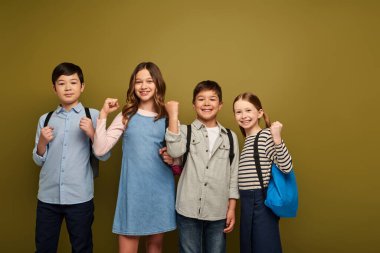 Sırt çantalı çoklu etnik gruplara mensup çocuklar. Güç gösterisi olarak yumruklarını gösteriyorlar. Dünya Çocuk Koruma Günü kutlamalarında kameraya bakıyorlar.