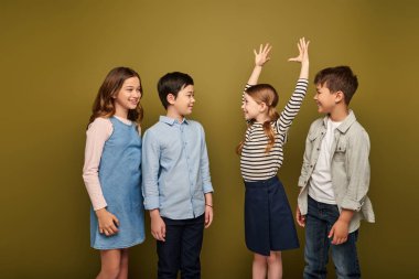 Gülümseyen kızıl saçlı kız ellerini kaldırmış, neşeli çoklu etnik arkadaşlarını işaret ediyor ve korkutuyordu. Bu arada haki rengi arka planda çocuk koruma gününü kutluyordu.