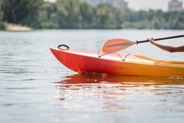 cropped view of hand of active african american woman with paddle sailing in sportive kayak on calm river during water recreation on summer weekend, summer fun clipart