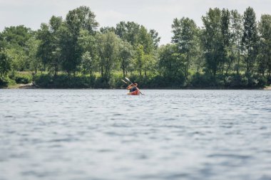 Aktif ve ırklar arası çiftlerin yaz tatilinde yeşil bankayla nehir kıyısında spor kanoyla yelek giyip yelek giymelerini izlemek.
