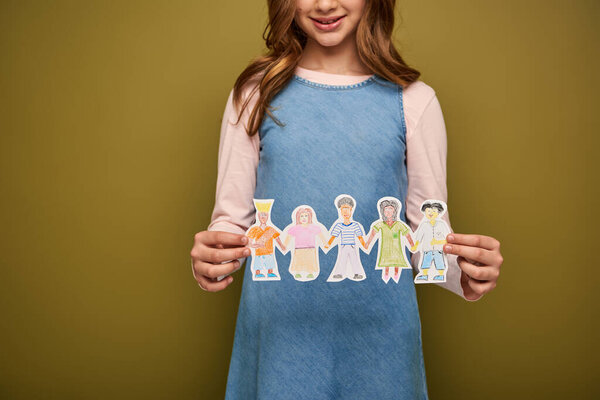 Cropped view of smiling preteen girl in casual clothes holding paper drawn characters during child protection day celebration on khaki background