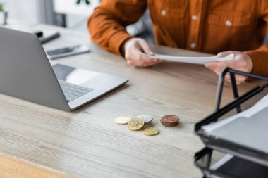 KYIV, UKRAINE - 18 Ekim 2022: Modern ofis çalışma masasında akıllı telefon, dizüstü bilgisayar, gümüş ve altın bitcoinlerin yanında duran şık gömlekli işadamının kırpılmış görüntüsü
