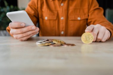 KYIV, UKRAINE - 18 Ekim 2022: Ofisteki çalışma masasında gümüş ve altın bitcoin 'lerin yanında otururken şık gömlekli girişimcinin kısmi görüşü