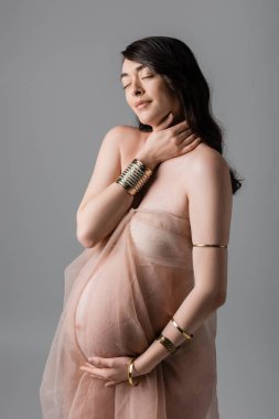 Çekici ve romantik bir anne olacak. Nazik şifon örtüler ve altın bilezikler takacak. Gri arka planda kapalı gözler duracak.