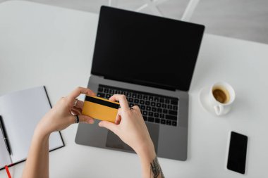 Dövmeli bir kadının elinde laptop, akıllı telefon, kalemli defter, beyaz masa üzerinde fincan fincan fincan kahve, modern çalışma alanı, evden çalışma 