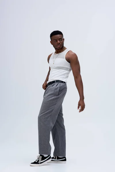 パンツやタンクトップスタンドで強力なアフロアメリカ人男性の完全な長さと灰色の背景にスタイリッシュでトレンディーな衣装で自信を持ってポーズ — ストック写真