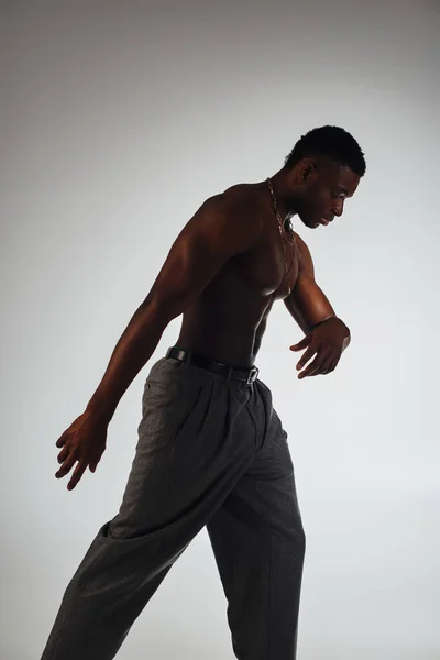 グレー 自信と現代的なポーズ ファッション撮影 無気力な男に隔離された影の中に立って灰色のパンツで筋肉アフリカ系アメリカ人モデルの側面図 — ストック写真