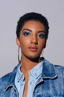Modayı takip eden Afro-Amerikan kadın portresi. Kalın makyajlı ve altın küpeli. Kot kıyafeti giymiş.