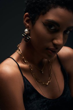 Akşam makyajlı ve altın aksesuarlı modacı Afro-Amerikan modelinin portresi. Işıkla izole edilmiş kameraya bakıyor.