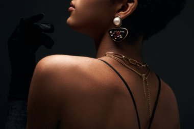 Zarif altın aksesuarları olan şık Afro-Amerikan modelinin siyah üzerinde aydınlık, yüksek moda ve akşam modasıyla tek başına dururken çekilmiş görüntüsü.