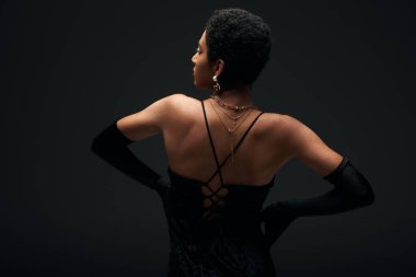 Zarif eldivenler ve altın aksesuarlarla siyah, yüksek moda ve akşam kıyafetleriyle izole edilmiş kalçalarda el ele tutuşan Afro-Amerikan kadınlarının yan görüntüsü.