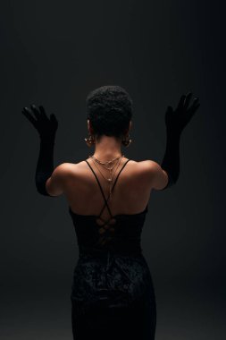Altın aksesuarları olan, siyah, yüksek moda ve akşam kıyafetleriyle poz veren modaya uygun Afro-Amerikan modelinin arkası.