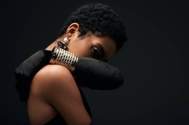 Aksesuar ve eldiven giyip siyah, yüksek moda ve akşam modasında izole edilmiş kameraya bakan şık Afro-Amerikalı kadın.