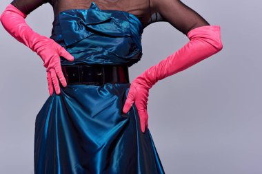 Cropped view of trendy young woman in cocktail dress and pink gloves touching hips and standing isolated on grey, modern generation z fashion concept, details, belt, feminine clipart