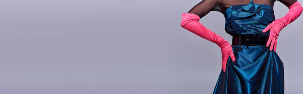 Cropped view of trendy young woman in cocktail dress and pink gloves touching hip and posing isolated on grey, modern generation z fashion concept, details, belt, feminine, banner 