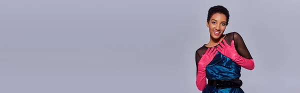 面带微笑的非洲美式模特形象 戴着粉色手套 身穿鸡尾酒裙 面带微笑 凝视着被灰色 现代流行观念 横幅隔离的相机 — 图库照片